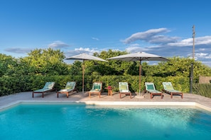A pool area with lounge chairs and umbrellas, surrounded by greenery. - Villa Linda - Noto - Siracusa (Noto)