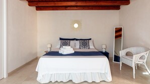 Un dormitorio con techo de madera, una cama con ropa blanca, dos lámparas de noche y una silla blanca.