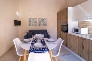 A modern kitchen with white cabinets, a microwave, and a dining area with a table set for four. - Villa Linda - Noto - Siracusa (Noto)
