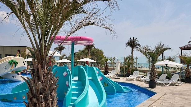 Un área de piscina con toboganes, sillas de descanso, sombrillas y palmeras.