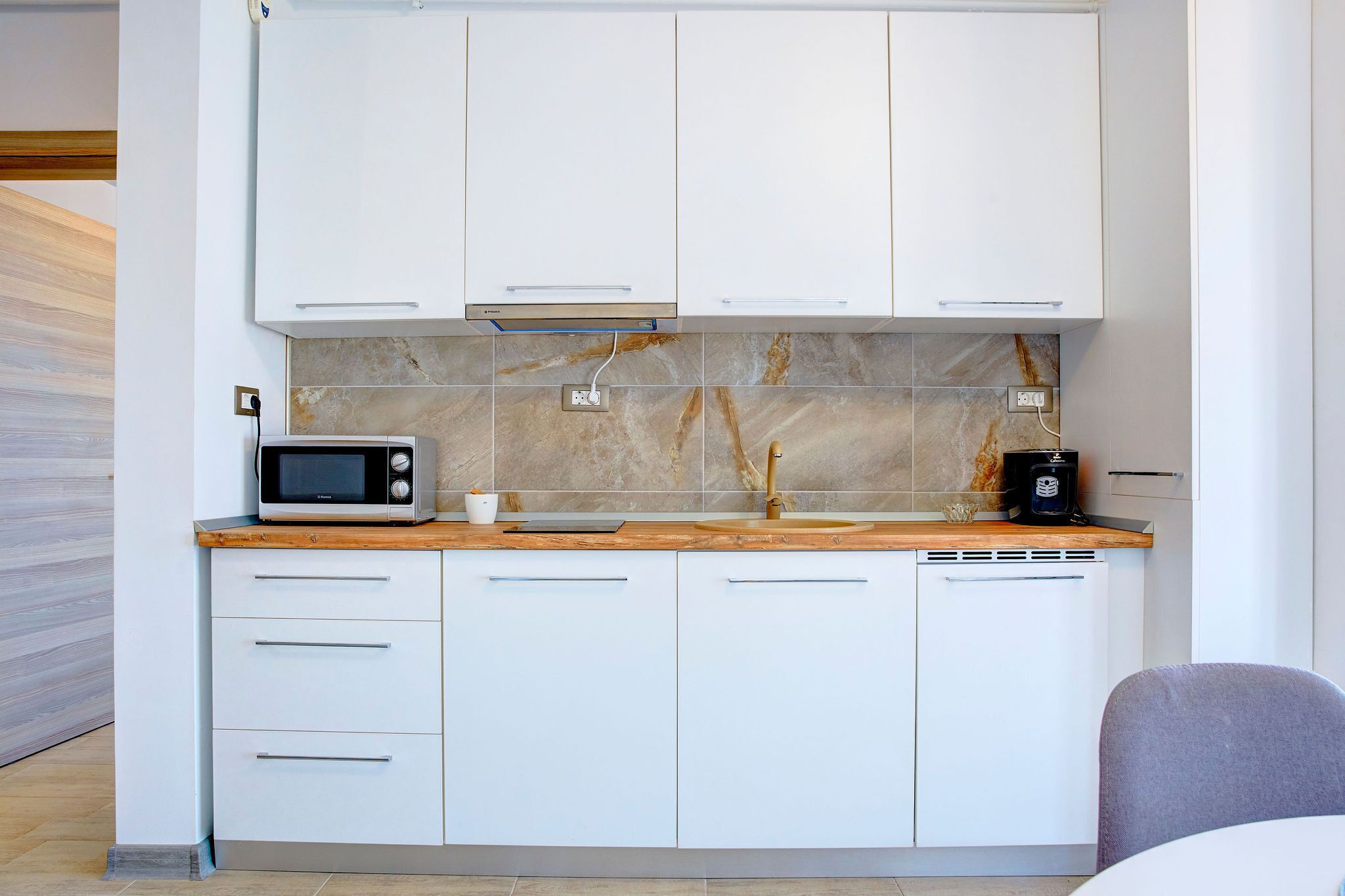 A compact kitchen with white cabinets, a microwave, a coffee maker, and a wooden countertop.