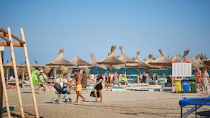 Una playa con sombrillas de paja, una estructura de madera y un letrero.