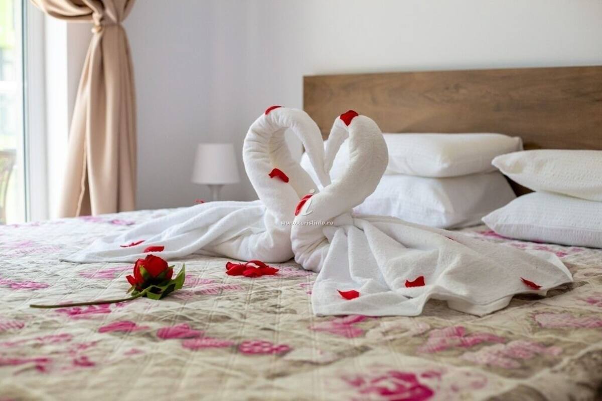 Una cama con toallas blancas dispuestas en forma de cisne, una rosa roja solitaria y una colcha con estampado floral.