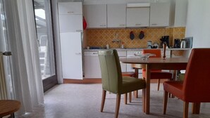 Une cuisine de taille réduite avec des meubles blancs, un pare-feu en carreaux et un coin repas comprenant une table et des chaises.