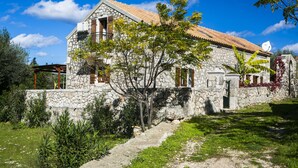 A stone building with a tiled roof, a satellite dish, and a small garden with a pathway leading to the entrance. - 1841 Petrino (Kefalonia)