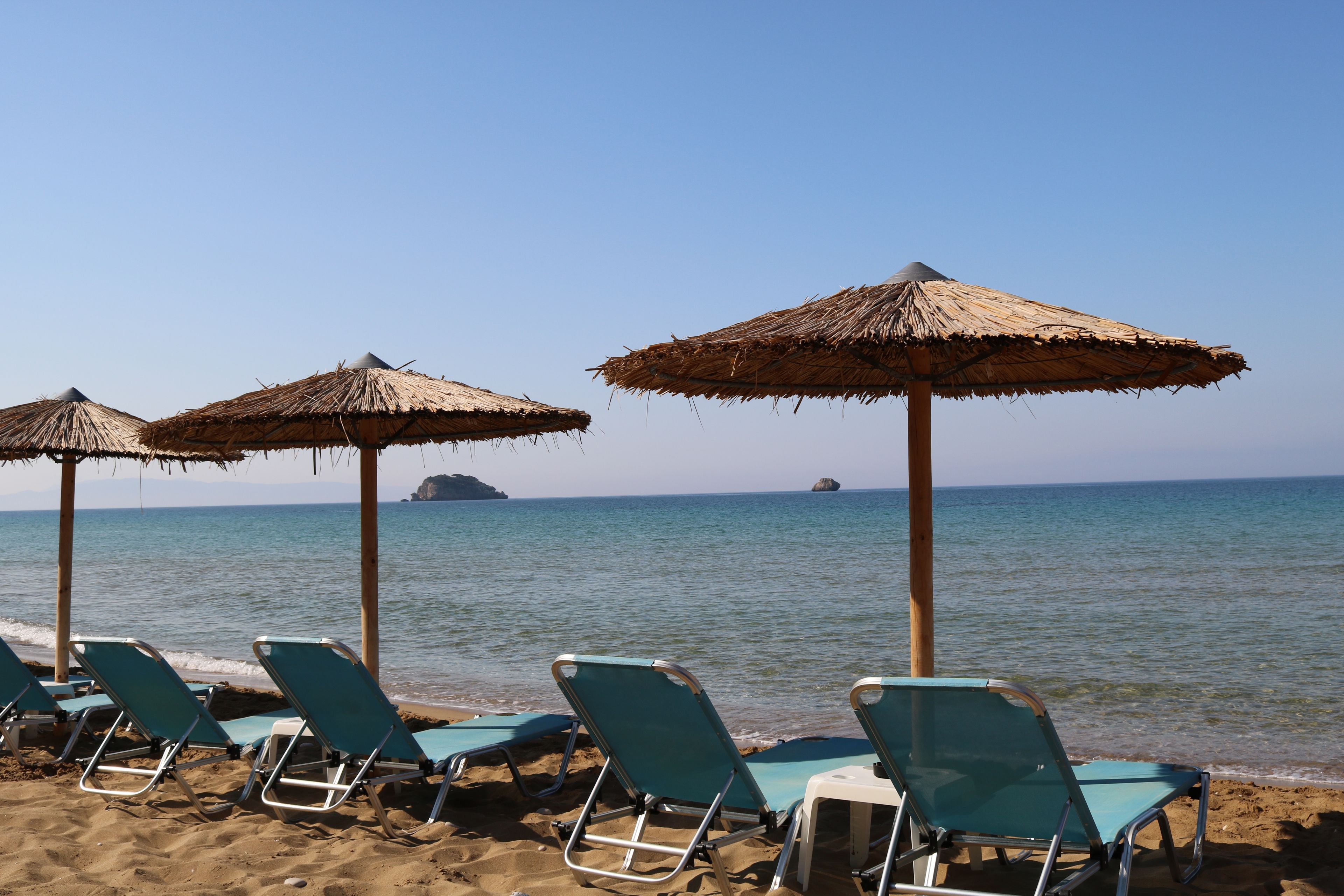 Beach chairs and thatched umbrellas on a sandy beach with the ocean in the background.