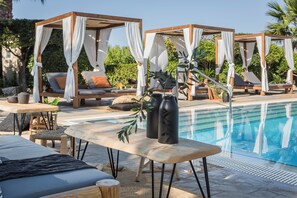 A poolside area with wooden loungers, a pool, and a pergola with white drapes. - Avithos Resort (Kefalonia)