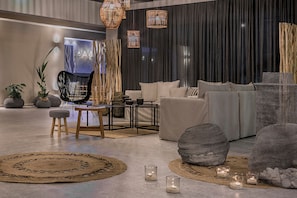 A modern living room with a sofa, chairs, and a coffee table. There are candles on the floor and a large painting on the wall. - Avithos Resort (Kefalonia)