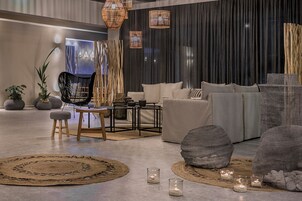 Un moderno salón con sofá, sillas y una mesa de centro. Hay velas en el suelo y un cuadro grande en la pared.