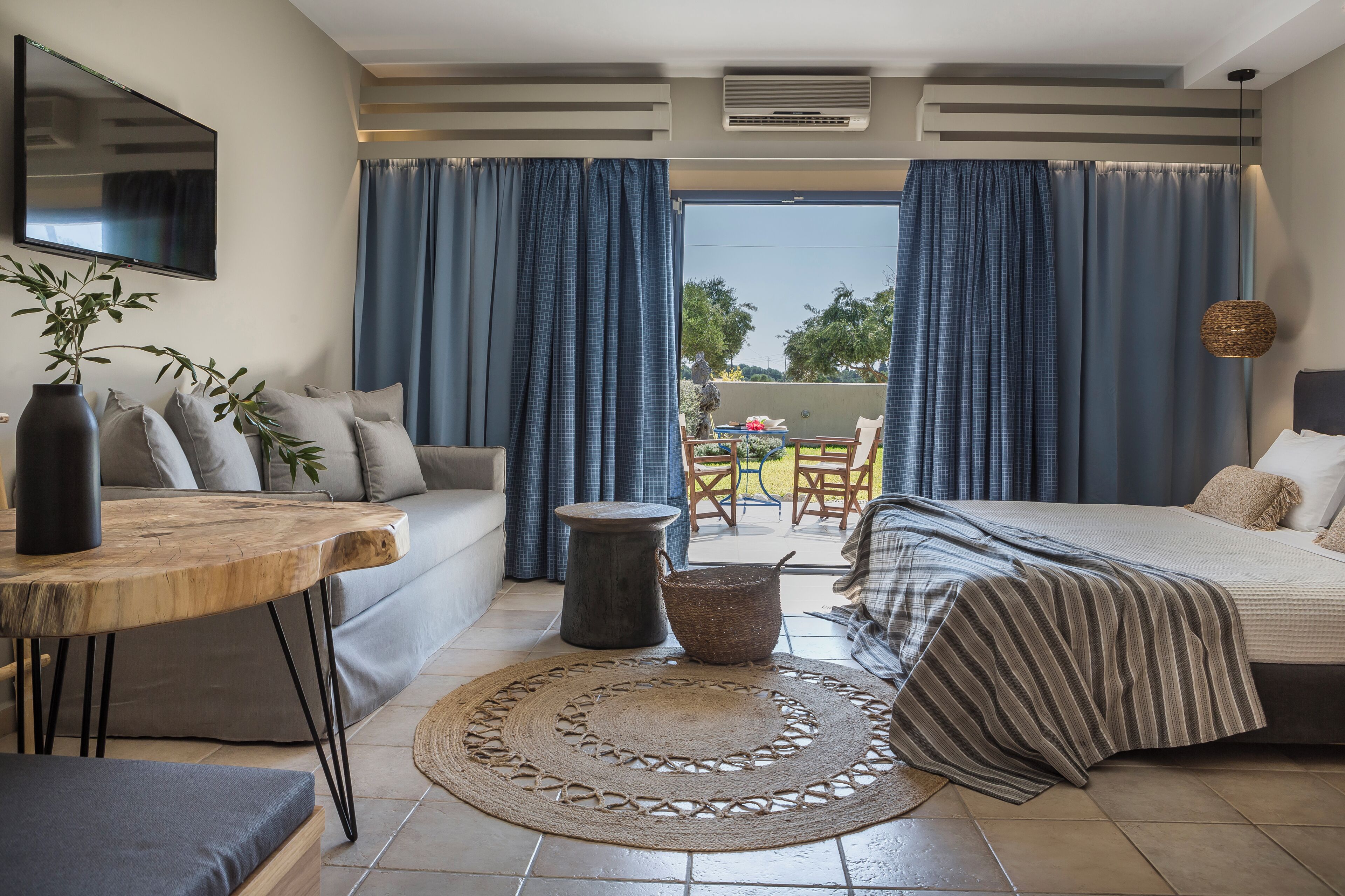 A bedroom with a bed, a sofa, a small table, a wicker basket, and a view through the curtains.