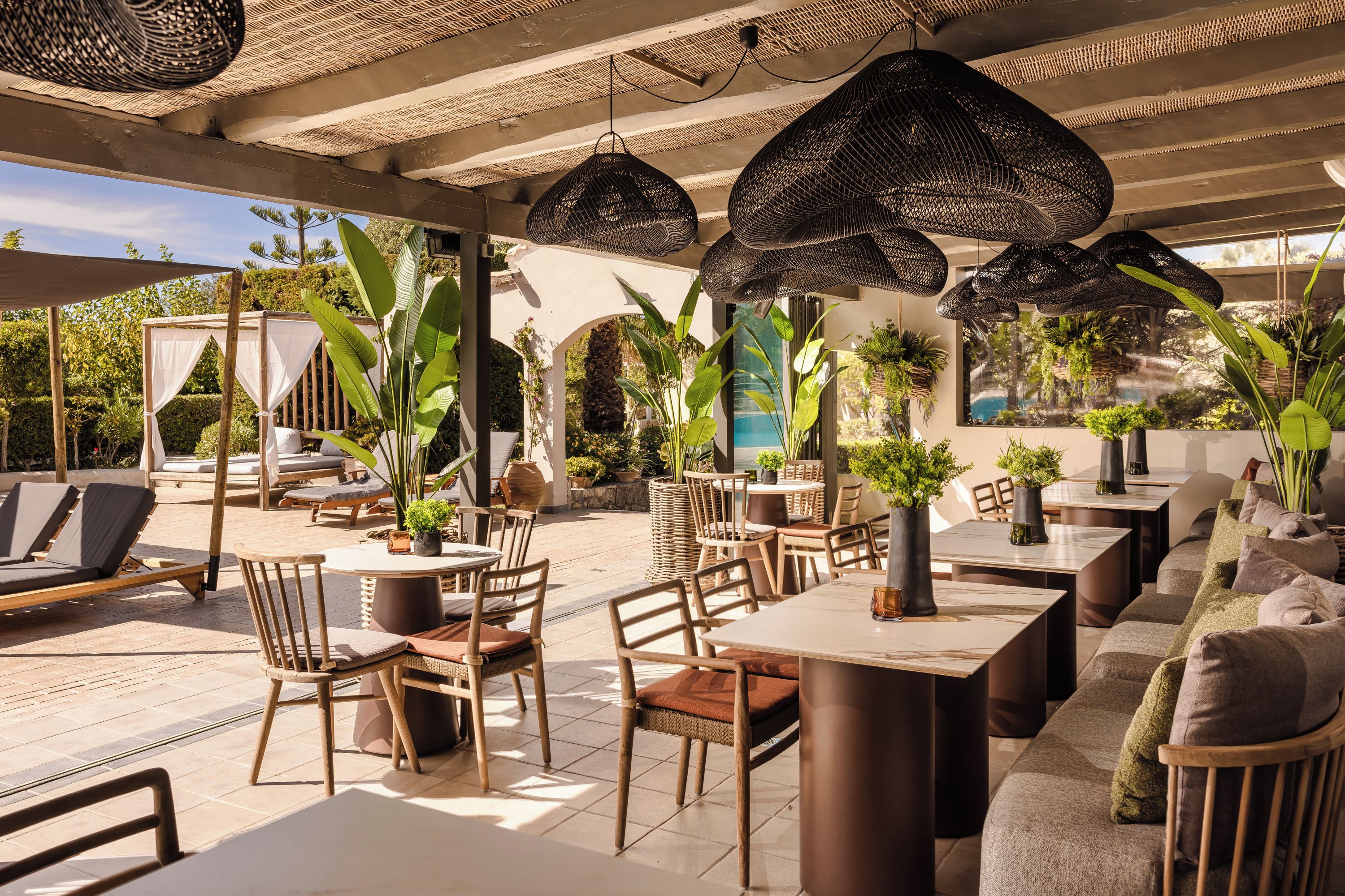 An outdoor patio area with wicker hanging lights, wooden furniture, and potted plants.