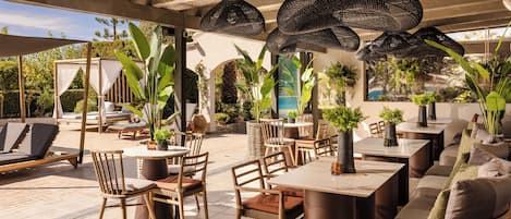An outdoor patio area with wicker hanging lights, wooden furniture, and potted plants.