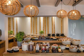 A buffet setup with various food items, wooden wall accents, and hanging wicker light fixtures. - Avithos Resort (Kefalonia)