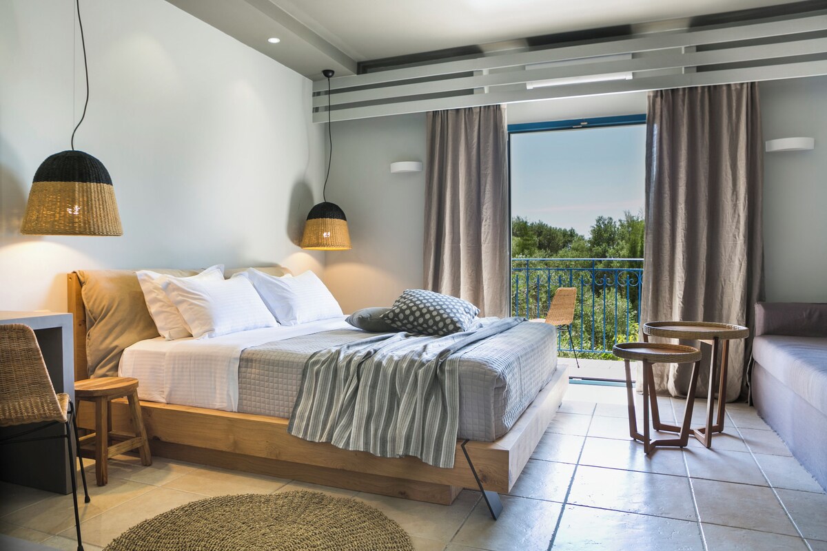 A bedroom with a bed, bedside tables, a chair, a small table, and a balcony with curtains.