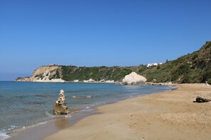 A beach with clear water, a rocky outcrop, and a hill with buildings. - Avithos Resort (Kefalonia)