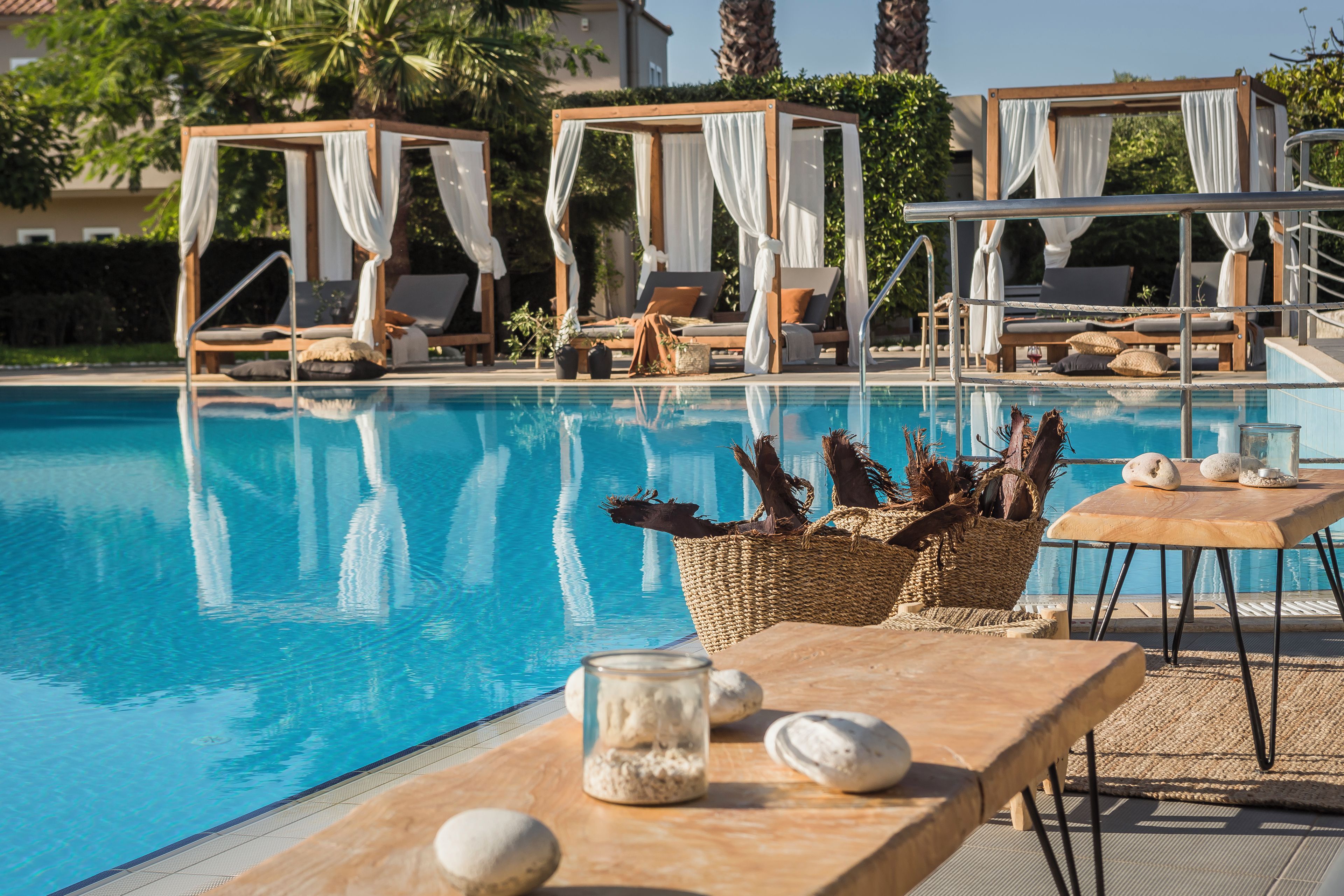 A poolside area with a clear blue pool, wooden lounge chairs, and a canopy structure.