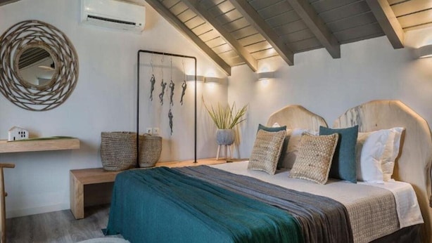 A bedroom with a bed, bedside tables, a wall-mounted air conditioner, a decorative mirror, and a wall art piece. - Avithos Resort (Kefalonia)
