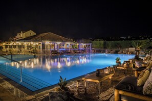 A swimming pool with a lounge area, outdoor seating, and a building with illuminated windows. - Avithos Resort (Kefalonia)