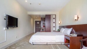 A hotel room with a bed, a TV mounted on the wall, a bedside table, and a chair. - Guang Xin Hotel (Shenzhen)