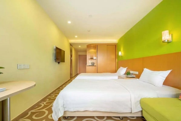 A hotel room with two beds, a small desk, and a television on the wall.