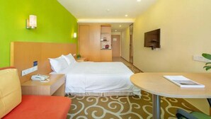 A hotel room with a bed, a bedside table with a phone, a small table with a book, a chair, and a TV on the wall. - Guang Xin Hotel (Shenzhen)