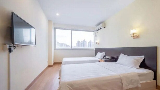 A hotel room with two beds, a TV, a window with a city view, and a wall-mounted light. - Guang Xin Hotel (Shenzhen)