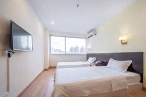 A hotel room with two beds, a TV, a window with a city view, and a wall-mounted light. - Guang Xin Hotel (Shenzhen)
