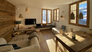 Ein gemütliches Wohnzimmer mit Holzwand, einer Couch, einem Esstisch und einem Fernseher.