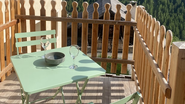 Eine Holzterrasse mit Tisch und Stühlen mit Blick auf eine gebirgige Landschaft.