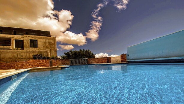 Una piscina amb aigua blava cristal·lina, envoltada per una paret de maó i un edifici blanc.