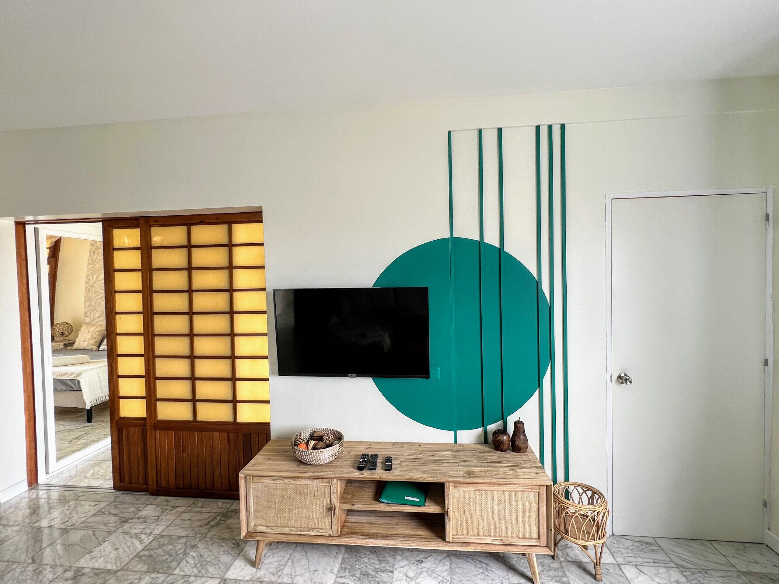 A modern living room with a TV mounted on the wall, a wooden cabinet with a woven basket, and a large decorative teal circle.
