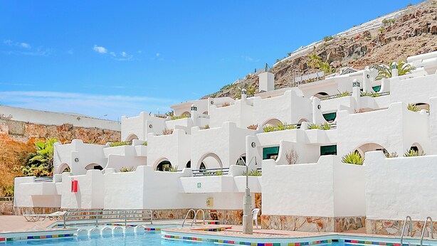 A pool area with white buildings and a clear blue sky. - Laguna Apartments (Mogan)