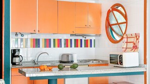 A kitchen with orange cabinets, a colorful backsplash, a toaster, and a coffee maker. - Laguna Apartments (Mogan)