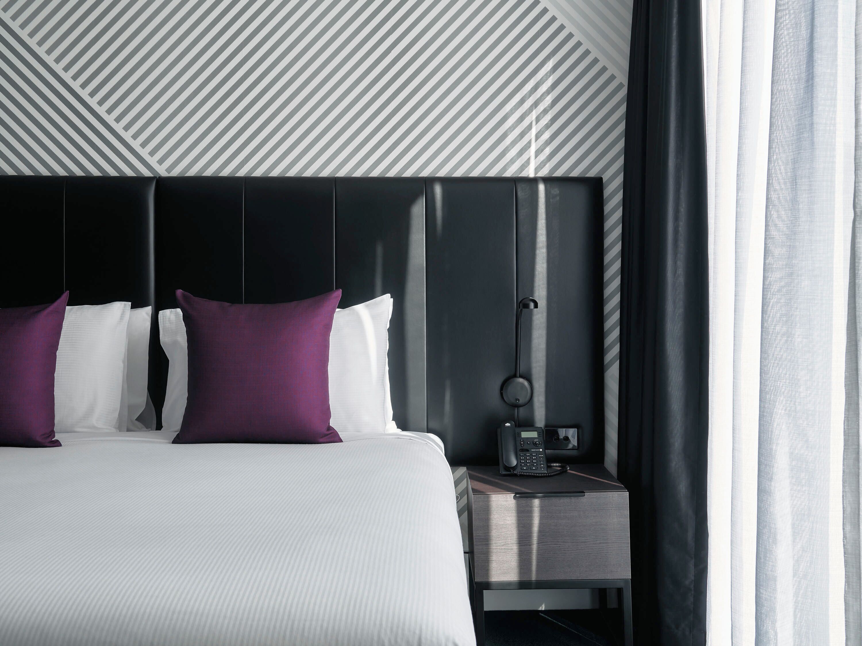 A modern hotel room with a large bed, a bedside table with a phone, and a geometric patterned wall.