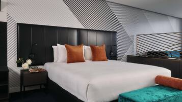 A modern hotel room with a large bed, a nightstand, a bedside table, and a decorative wall panel.
