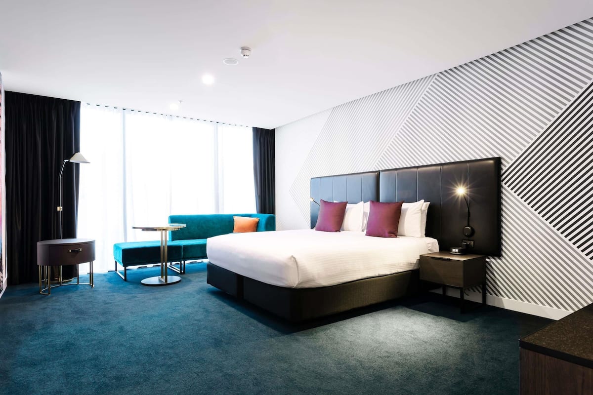Una habitación de hotel moderna con una cama grande, un sofá, una mesita y un televisor.