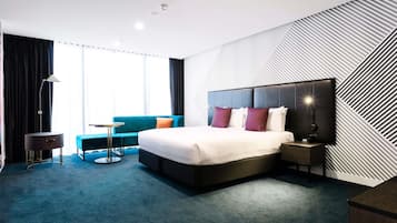 A modern hotel room with a large bed, a sofa, a small table, and a TV.