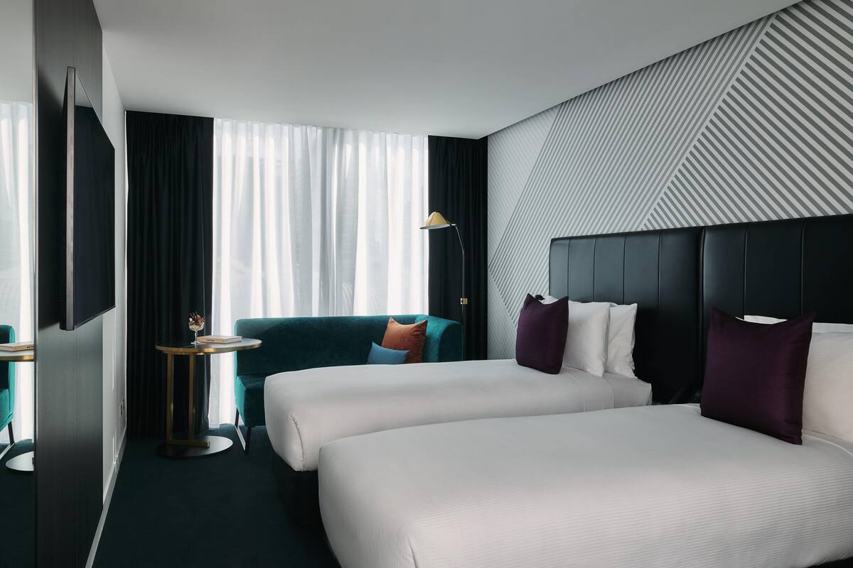 Habitación de hotel con dos camas, un escritorio, una silla, un televisor y un ventanal con cortinas.