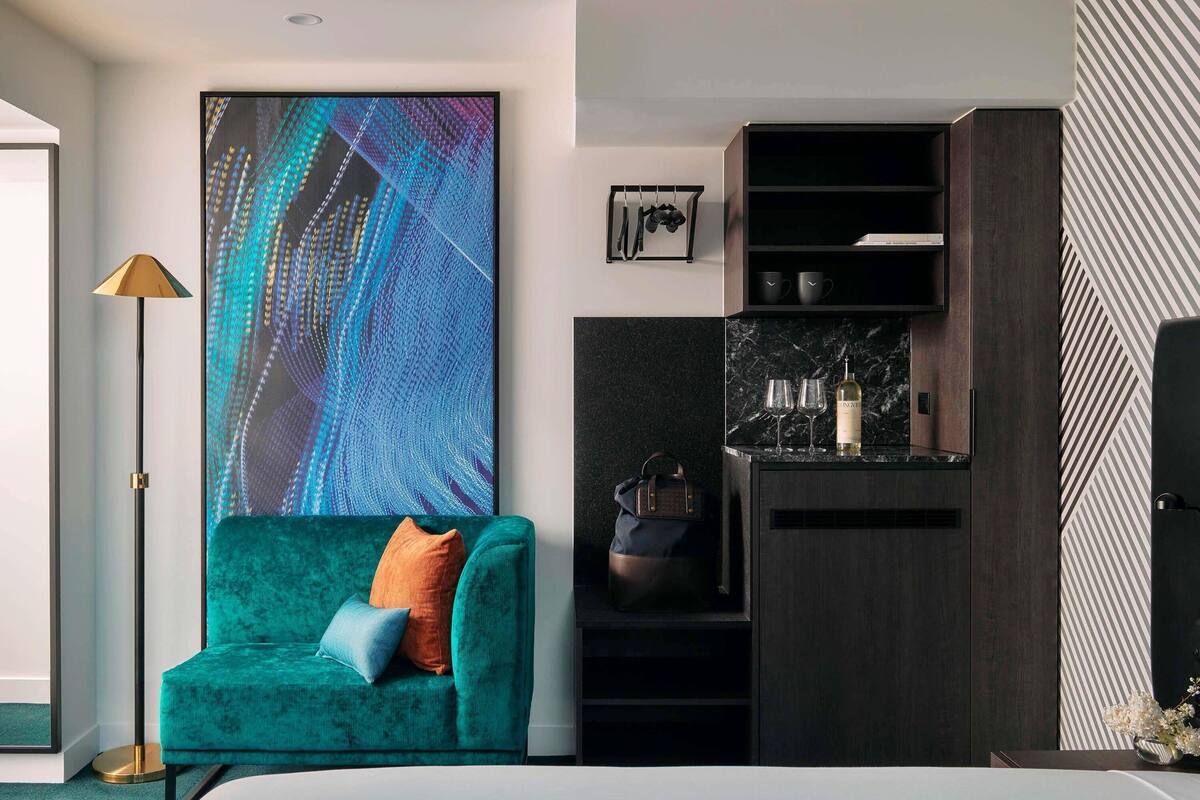 Una sala moderna con un sofá color turquesa, un cuadro abstracto grande, una lámpara de pie, un mueble de madera oscura y una cocina con encimera de mármol.