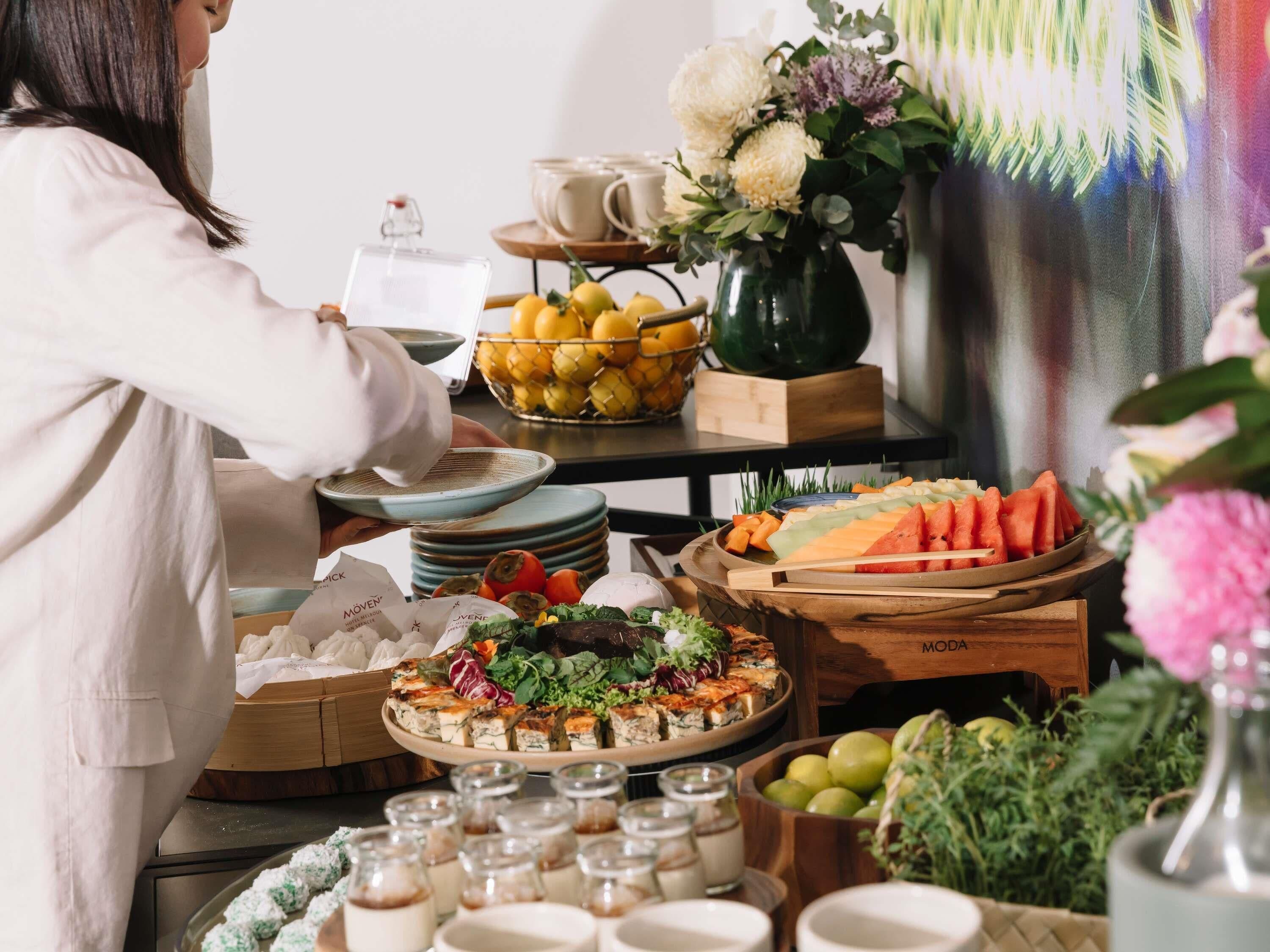 A buffet setup with various food items, a vase with flowers, and a person serving.