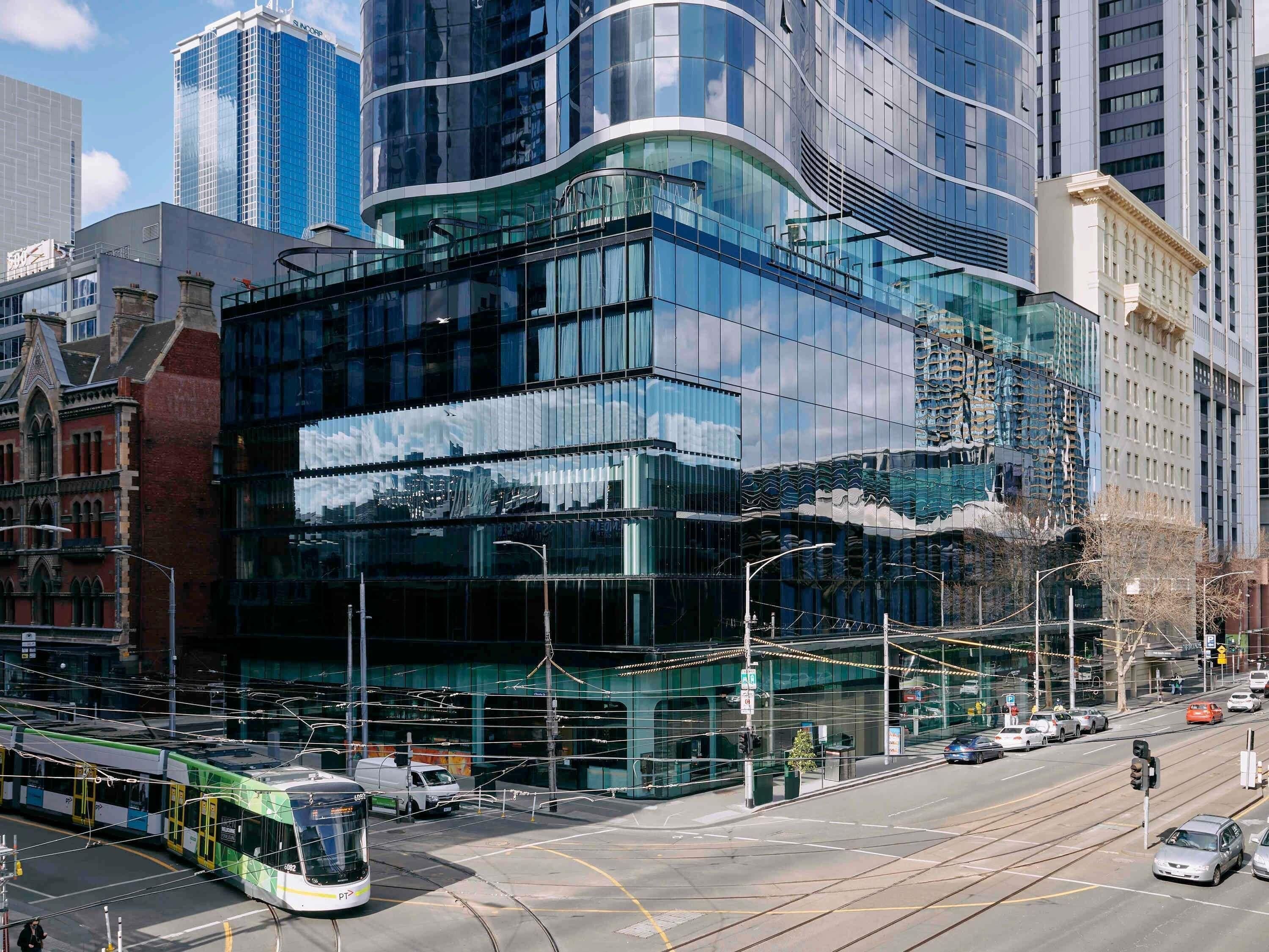 A modern building with large glass windows, a tram line, and a street with cars.