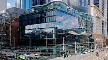 A modern building with large glass windows, a tram line, and a street with cars.