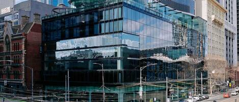 Un edificio moderno con amplios ventanales, una línea de tranvía y una calle con automóviles.