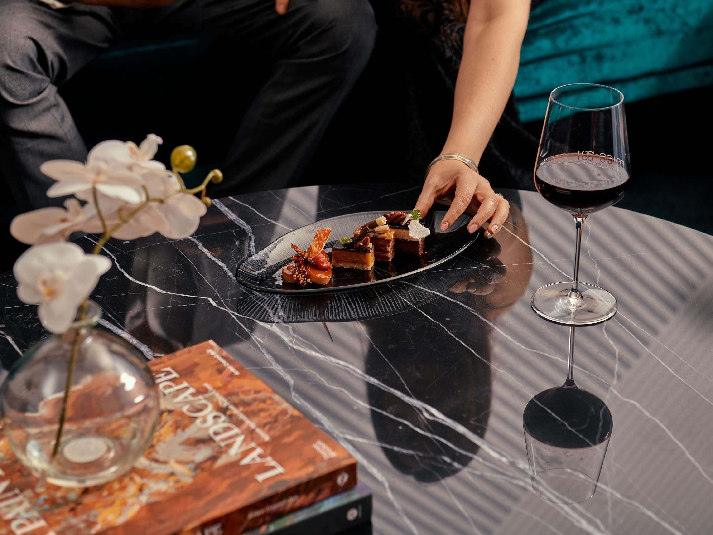 Uma mesa com um prato de sobremesa, uma taça de vinho e um livro intitulado "LANDSCAPE".