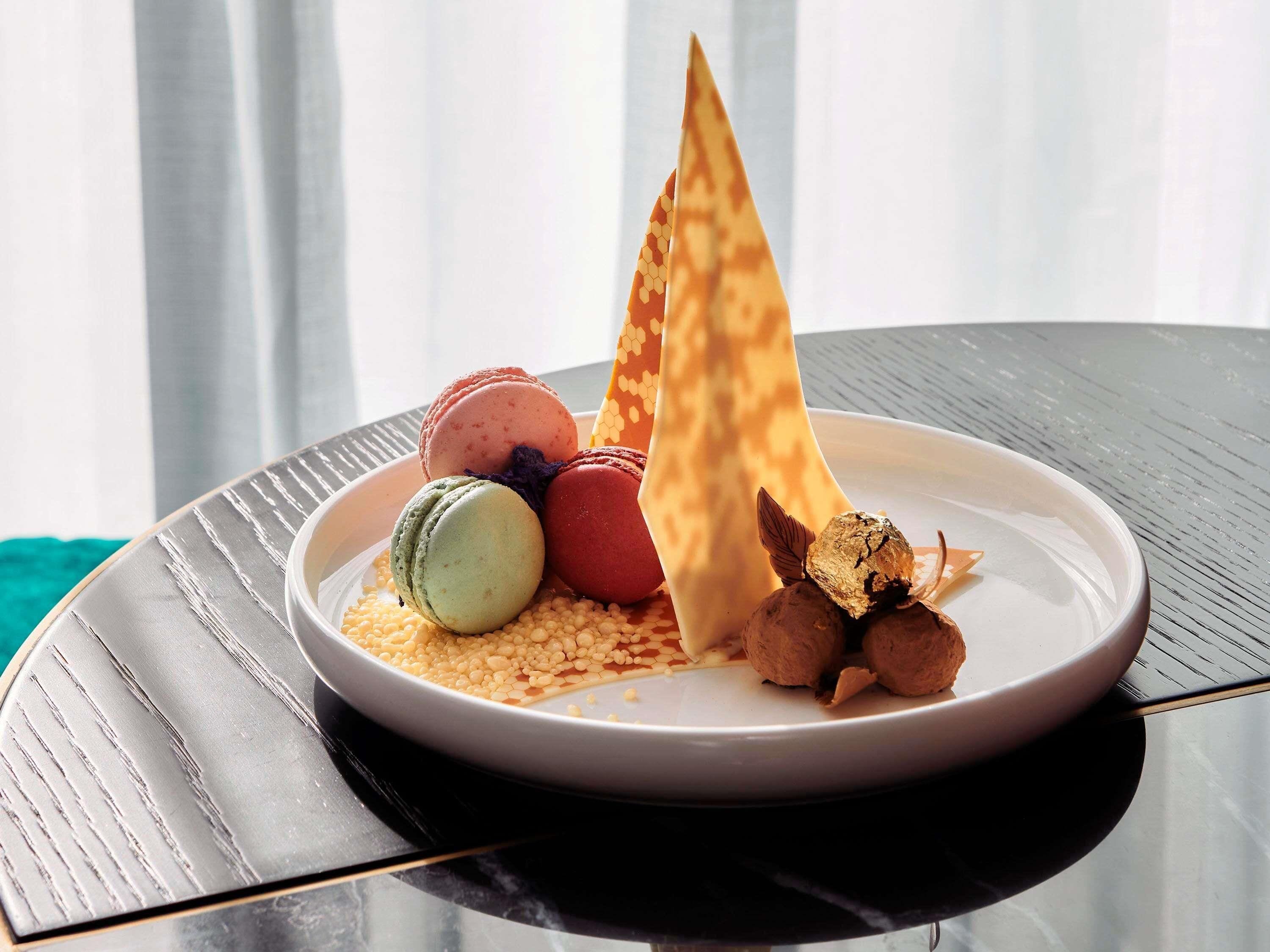 Un plato con macarons, un cono de gofre y trufas de chocolate sobre una mesa.