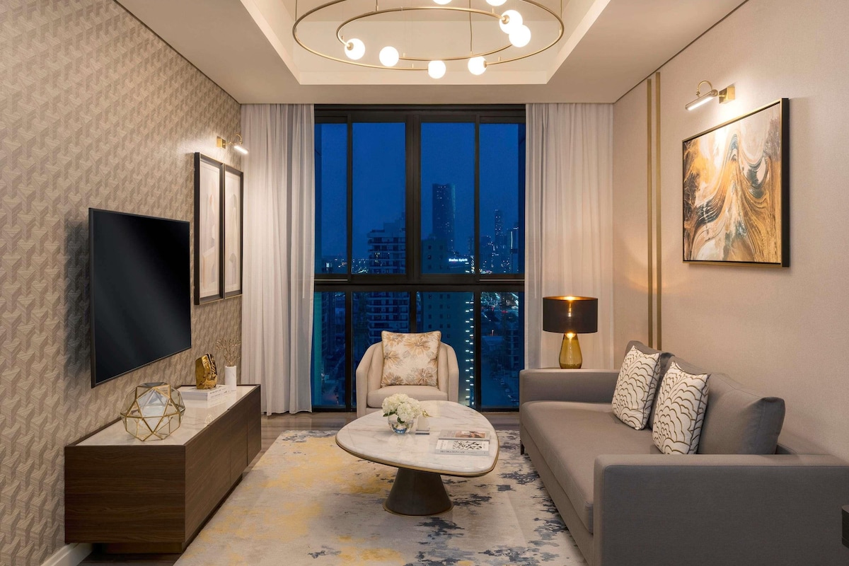 A modern living room with a TV, sofa, and a large window with a city view.