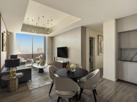 A modern living room with a dining area, a flat-screen TV mounted on the wall, and a large window offering a city view.
