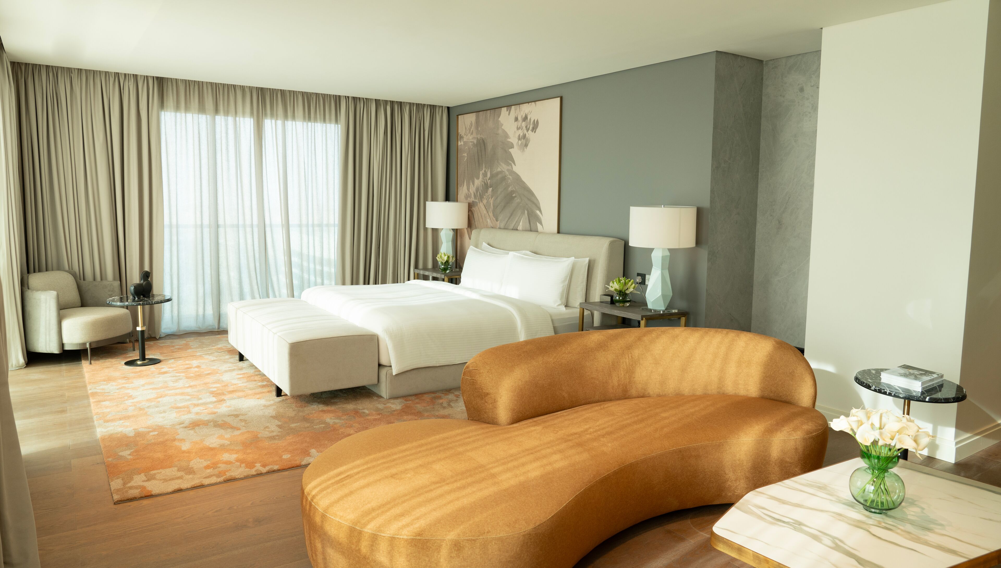 Una habitación de hotel moderna con una cama grande, un sofá, una mesita pequeña y una mesita de noche con lámparas.