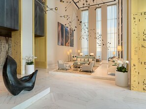 Un hall d’entrée spacieux au design moderne, comprenant un grand espace salon, une sculpture noire originale et de grandes fenêtres laissant entrer la lumière naturelle.