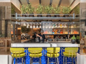 A bar area with a counter, bar stools, hanging lights, and potted plants.